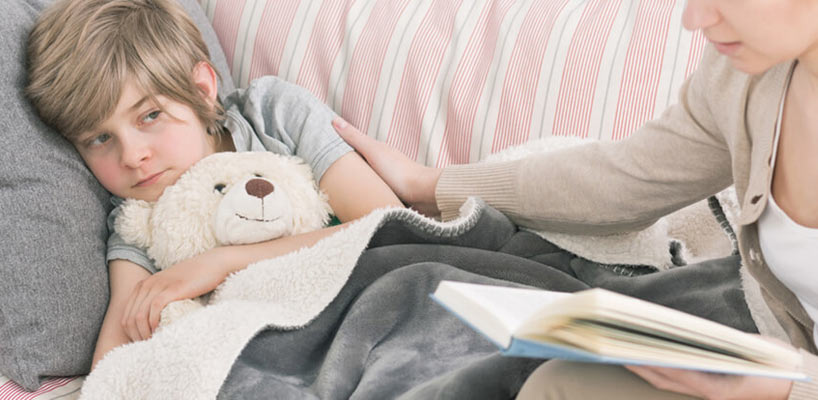 syg dreng ligger i sofa med tøjbamse